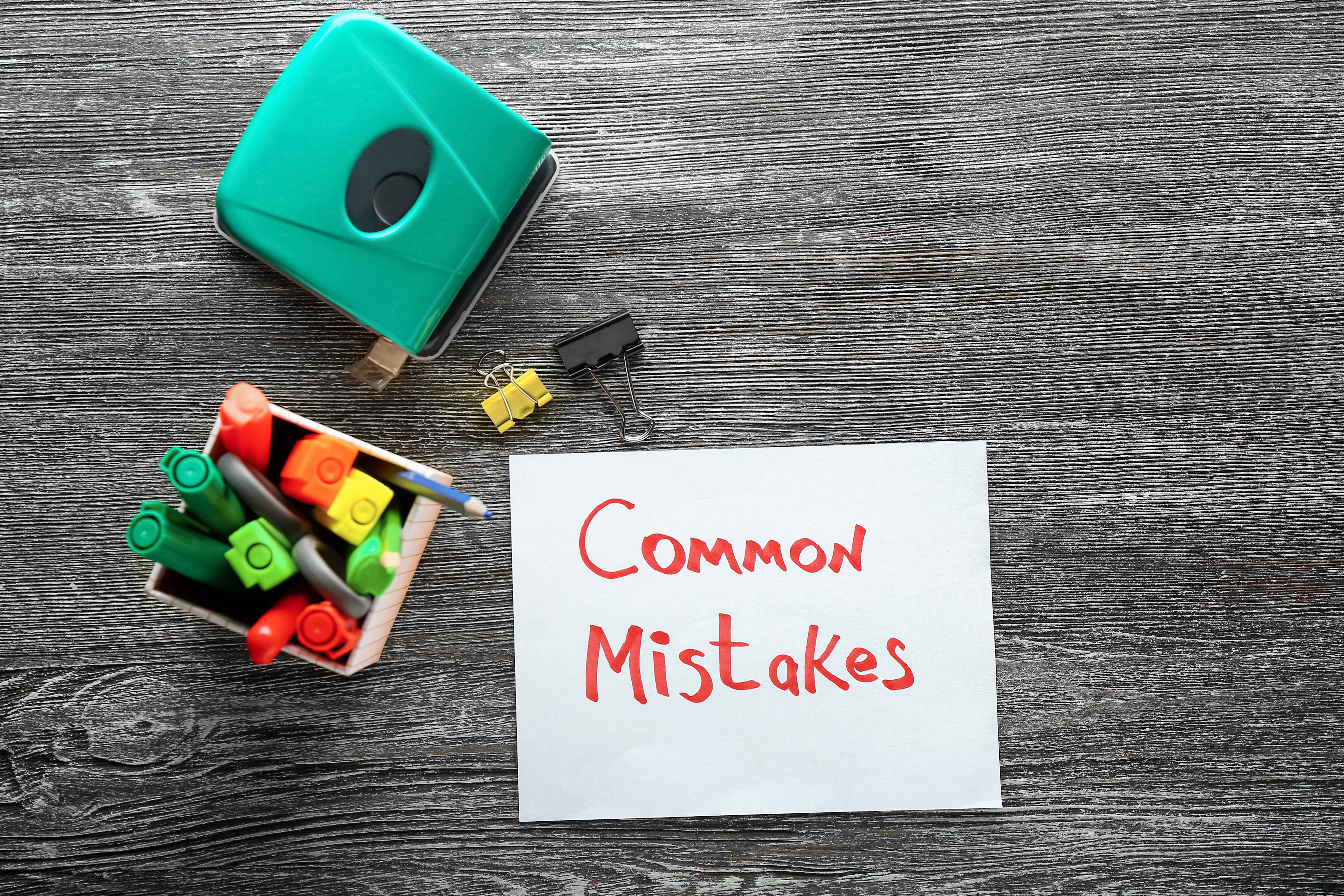 Stationery and sheet of paper with text COMMON MISTAKES on wooden background