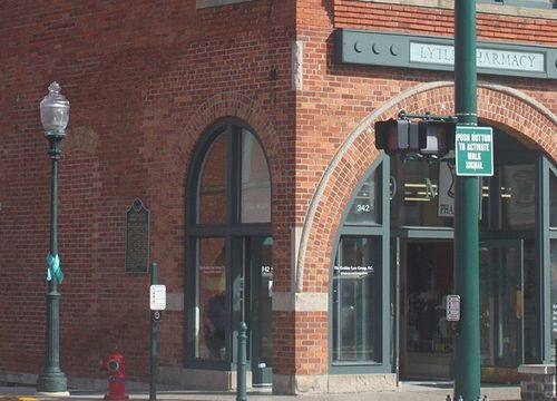 The image shows the exterior of Lytle Pharmacy, a brick building with arched windows and doorways