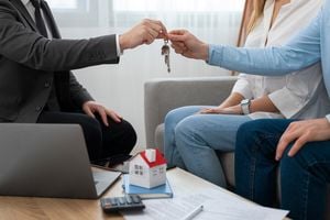 A man is handing keys to a couple who are seated on a sofa