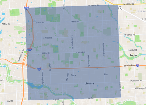 The image shows a street in Milford, Michigan, with traffic lights, shops, and parked cars