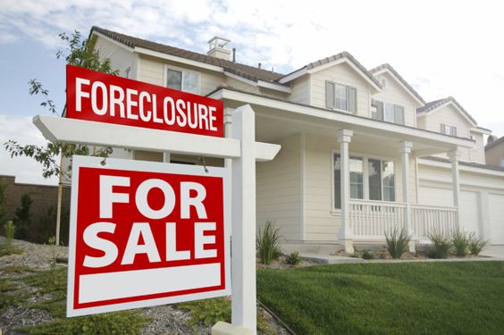 Signboard reading 'Foreclosed Home for Sale' placed in front of a white house