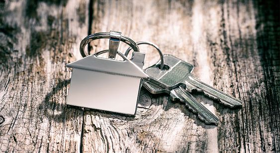 Key chain featuring a house-shaped charm resting on a rustic wooden board