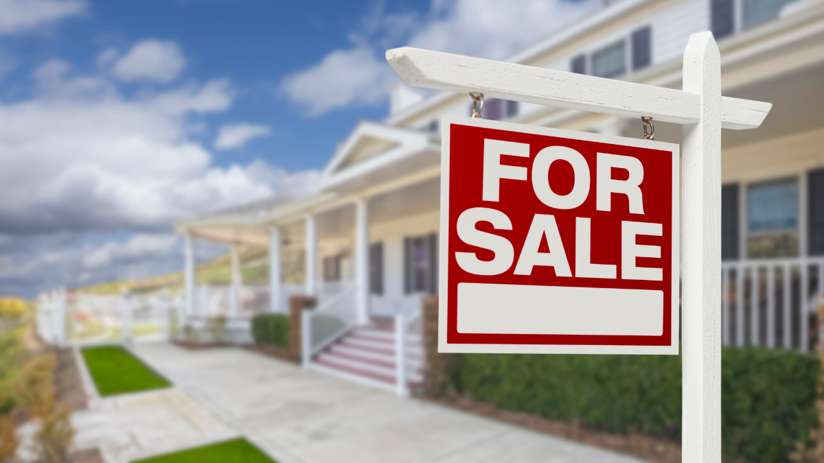 A bright red "For Sale" sign in front of a beautiful suburban home in Oakland County, MI, representing available homes for sale