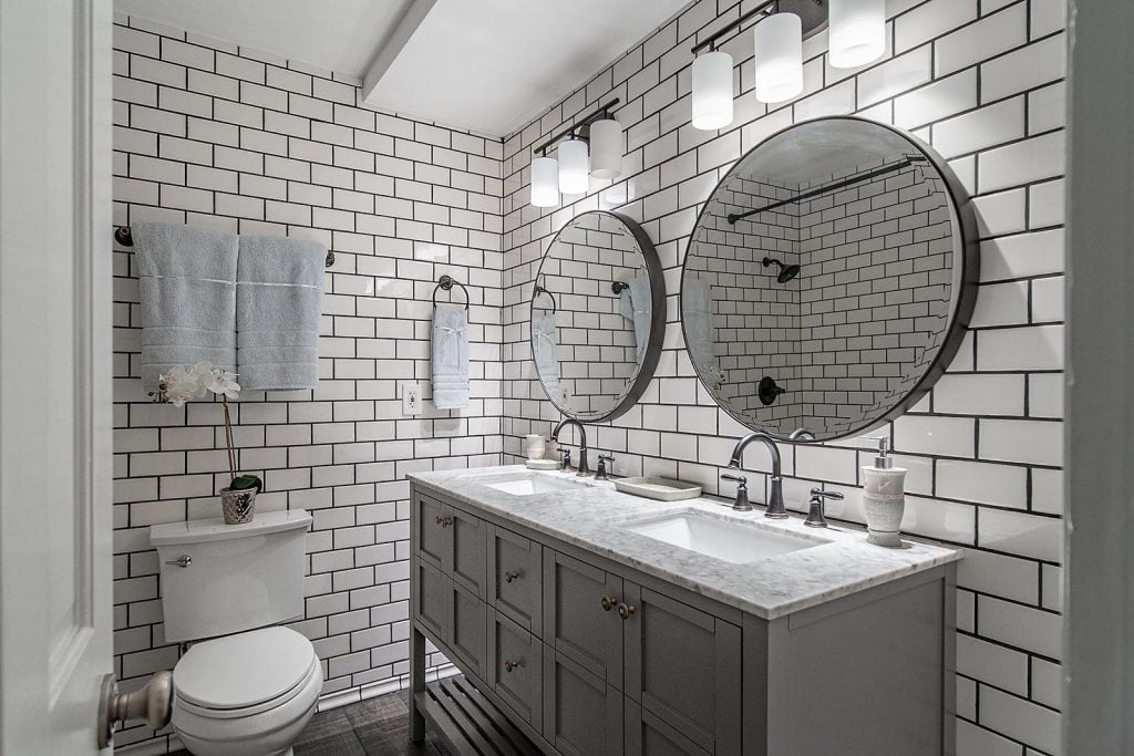 Bathroom with White Subway tiles, round mirrors, and gray cabinets.