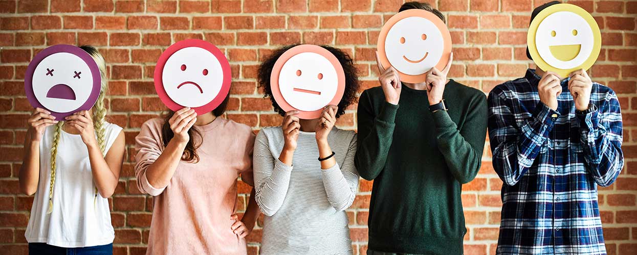 People standing in front of brick wall, holding paper faces with different emotions