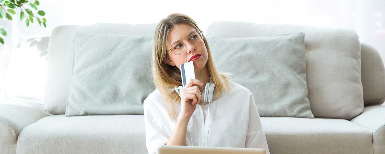 Woman sitting on floor in front of couch with credit card thinking about the costs of home ownership