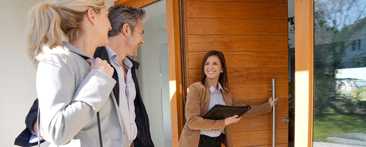 Realtor opening the front door of house for a man and woman