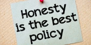 Sticky note thumbtacked to particle board that says "honesty is the best policy"