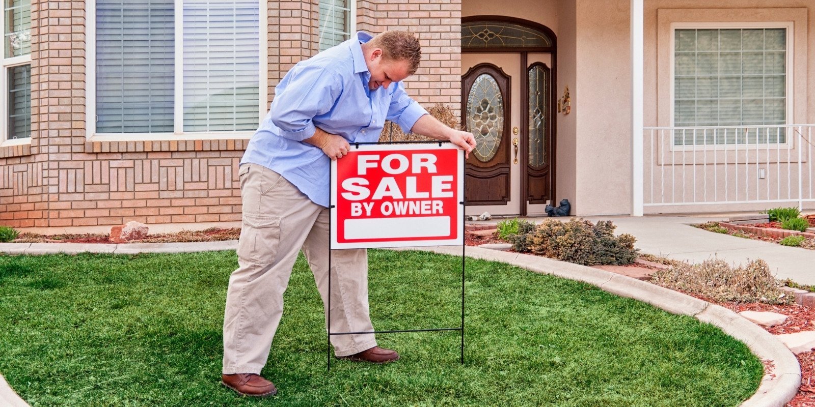 Man placing a For Sale By Owner sign in front yard