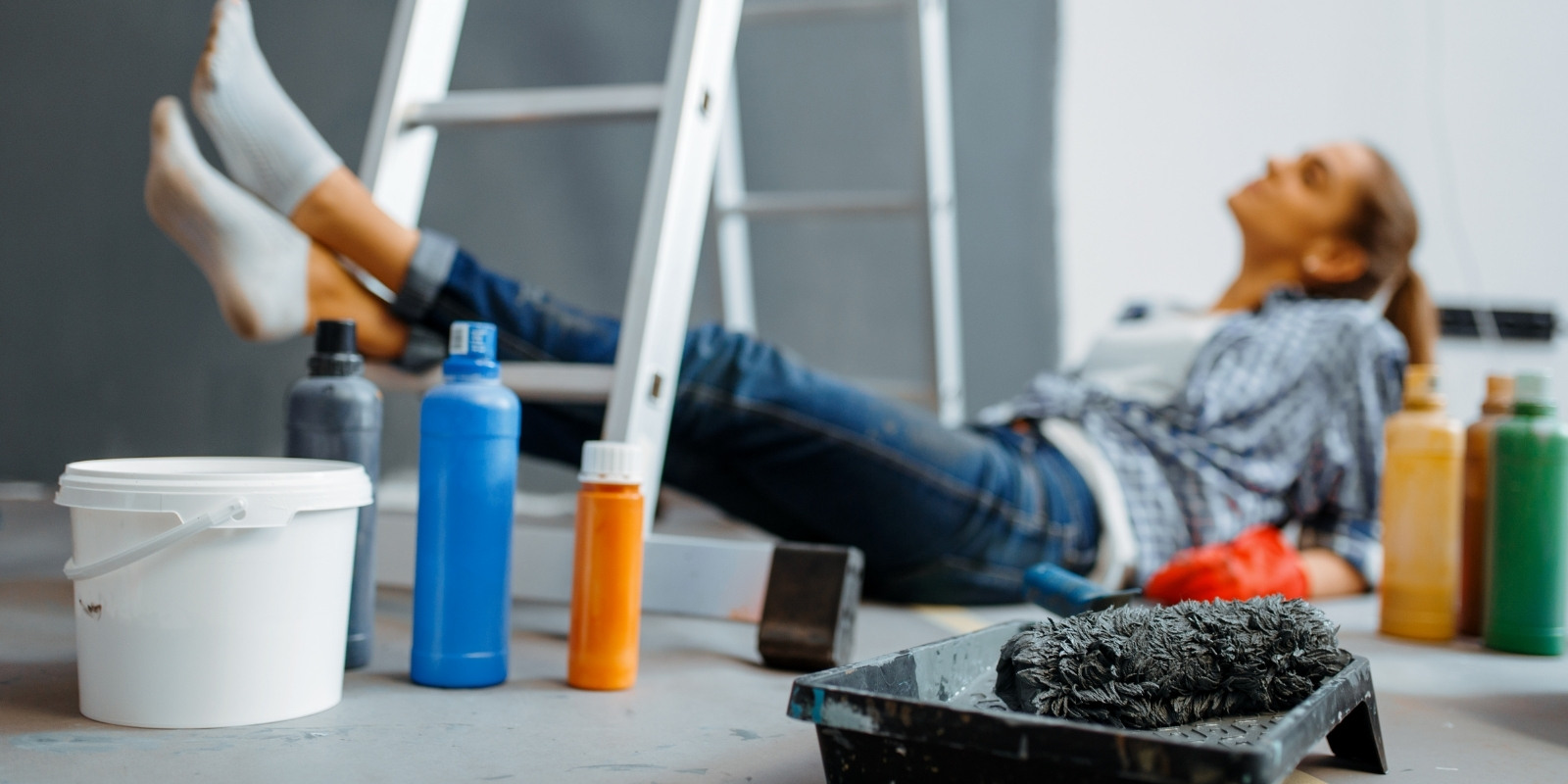 Woman laying down and resting her legs on a ladder, ignoring the repairs that her house needs