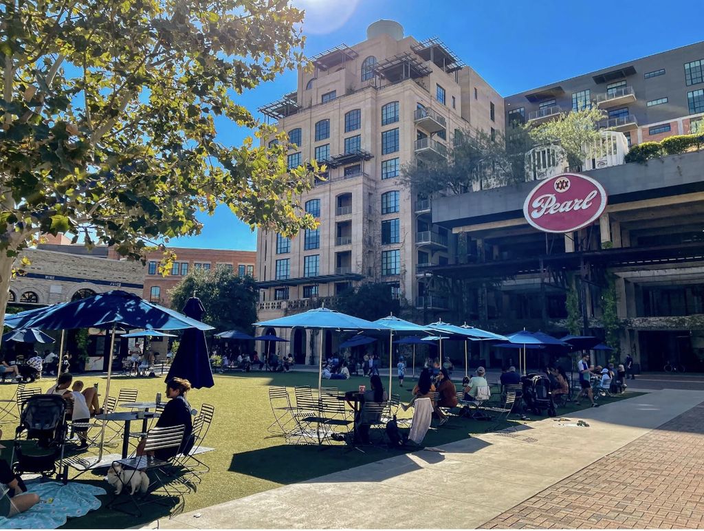 An outdoor photograph of the lawn at the Pearl District. Including tables with blue umbrellas.