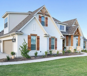 White Farmhouse with beautiful wooden shutters and mature landscaping out front