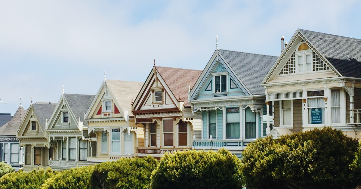 Row of colorful Victorian-style homes with intricate detailing, set against a bright sky.