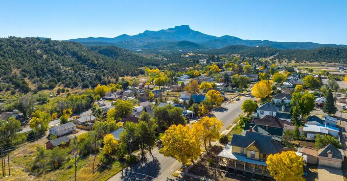 Aerial view of Trinidad, Colorado during the fall, with vibrant yellow trees, a quaint neighborhood, and distant mountains under a clear blue sky.