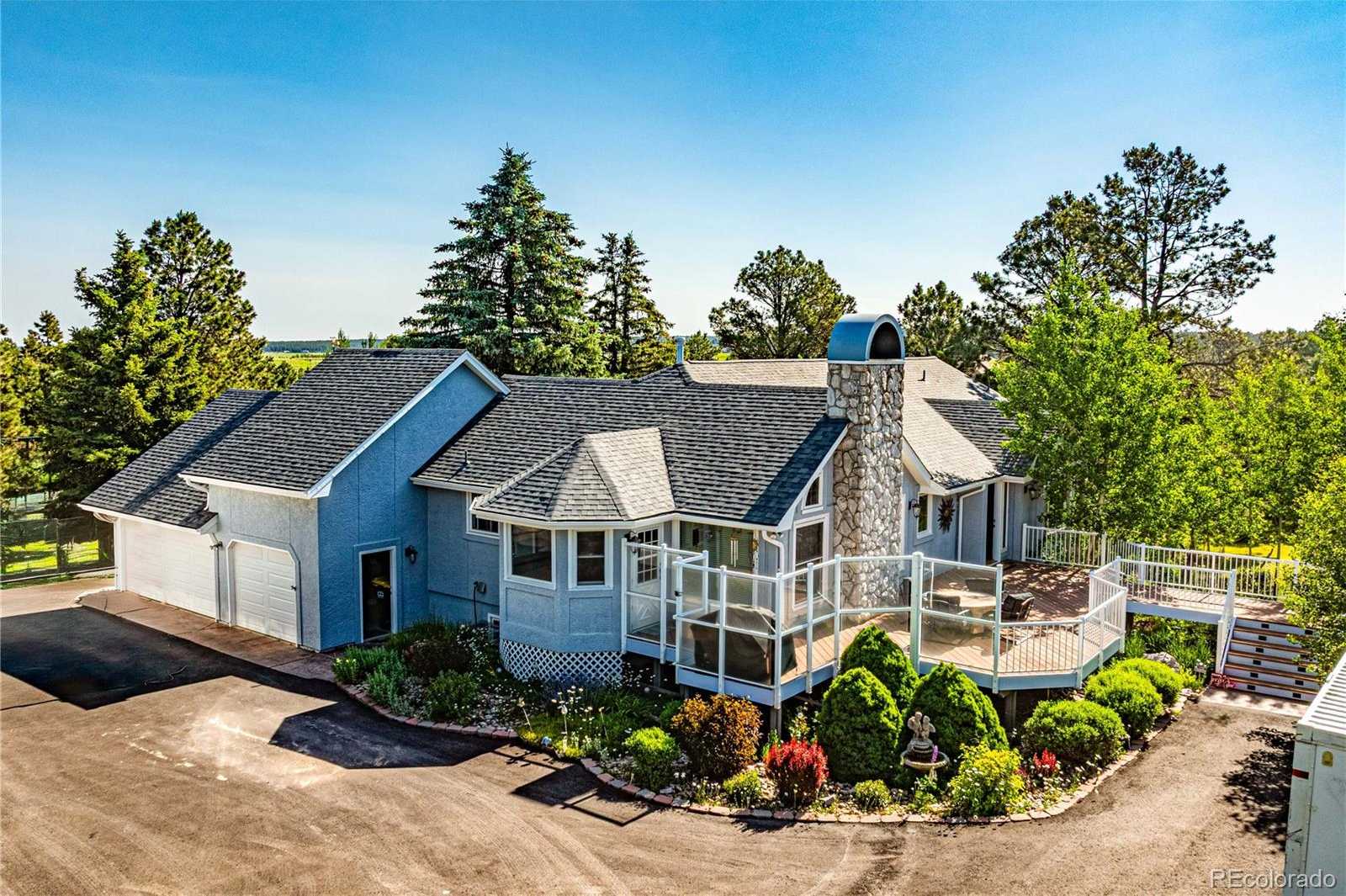 Exterior view of a custom ranch-style home with wraparound deck and mature trees in Monument, Colorado