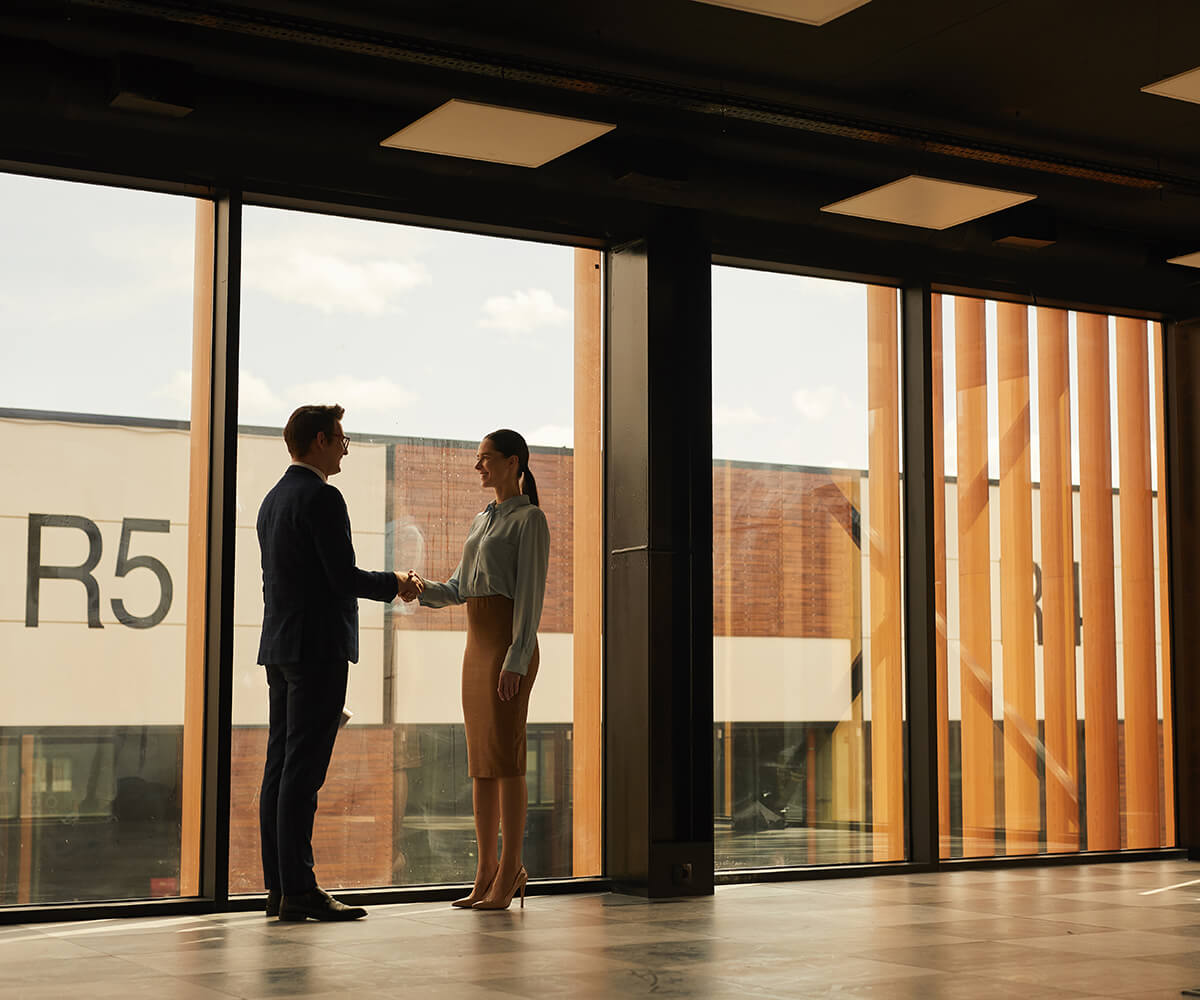 Wide-angle-view-of-real-estate-agent-shaking-hands-with-client-while-standing-in-empty-office-building