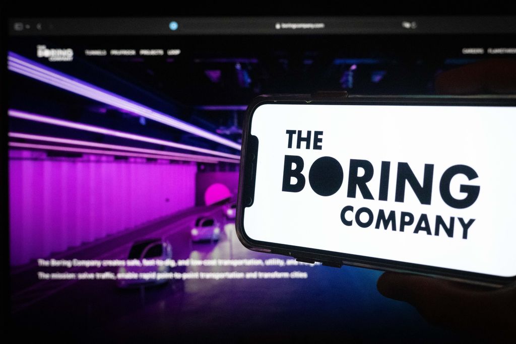 The Boring Company logo displayed on a smartphone screen with an illuminated tunnel interior visible in the background