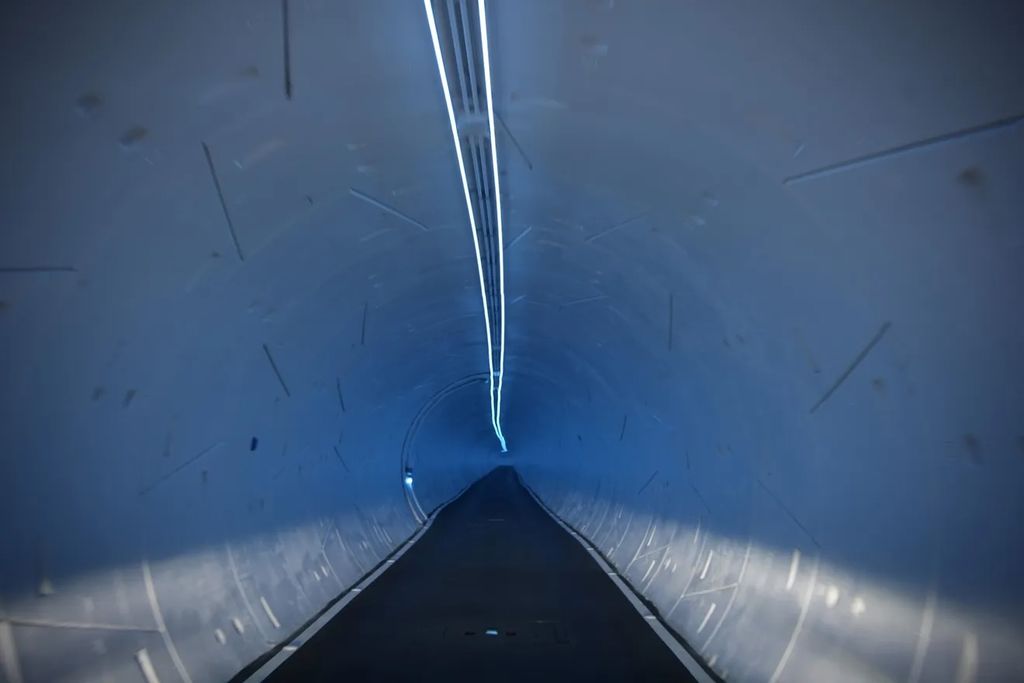 Interior view of a Boring Company underground tunnel with blue LED lighting showing the circular tunnel structure and single lane roadway