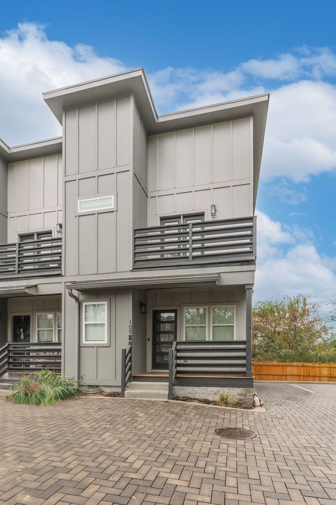 Exterior of 109 E Duke St Nashville TN, a 2023 modern gray board and batten end-unit townhome in East Nashville featuring a second-floor balcony, black metal railings, and paver driveway, listed by BDG Partners at Compass