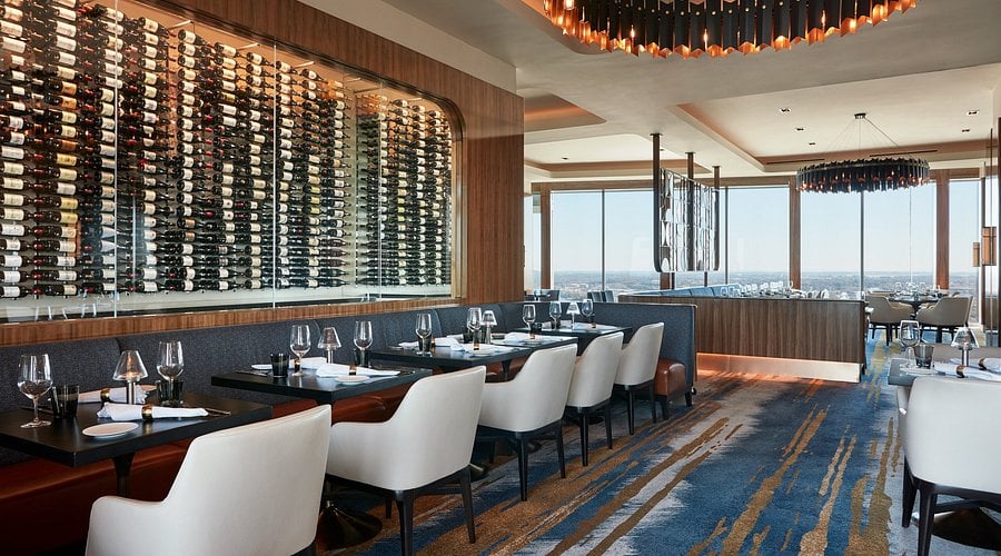 Interior of Bourbon Steak Nashville in The Gulch, featuring a floor-to-ceiling wine wall, white upholstered dining chairs, and panoramic skyline views