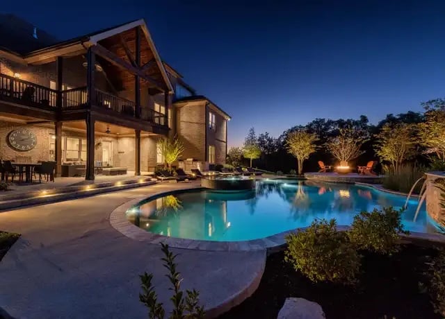 Evening view of a luxury Nashville home with illuminated outdoor pool, covered porch, and landscaped yard
