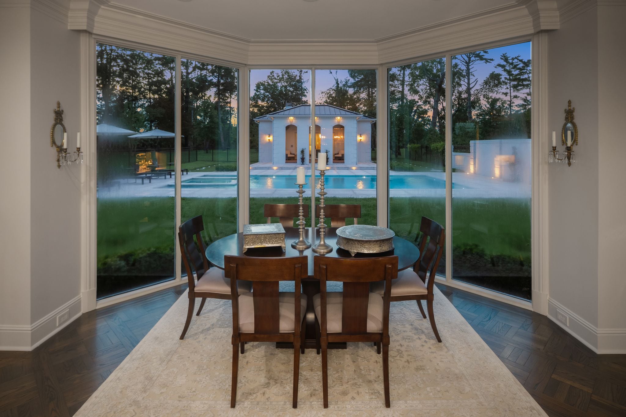 Breakfast room at dusk with panoramic windows overlooking the illuminated pool and pool house at 4753 Post Road, Nashville