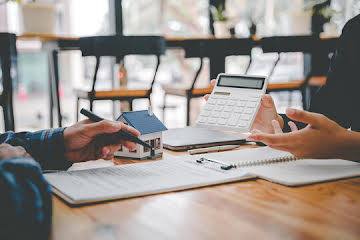 Calculator, model house, and documents representing housing market and mortgage forecasts
