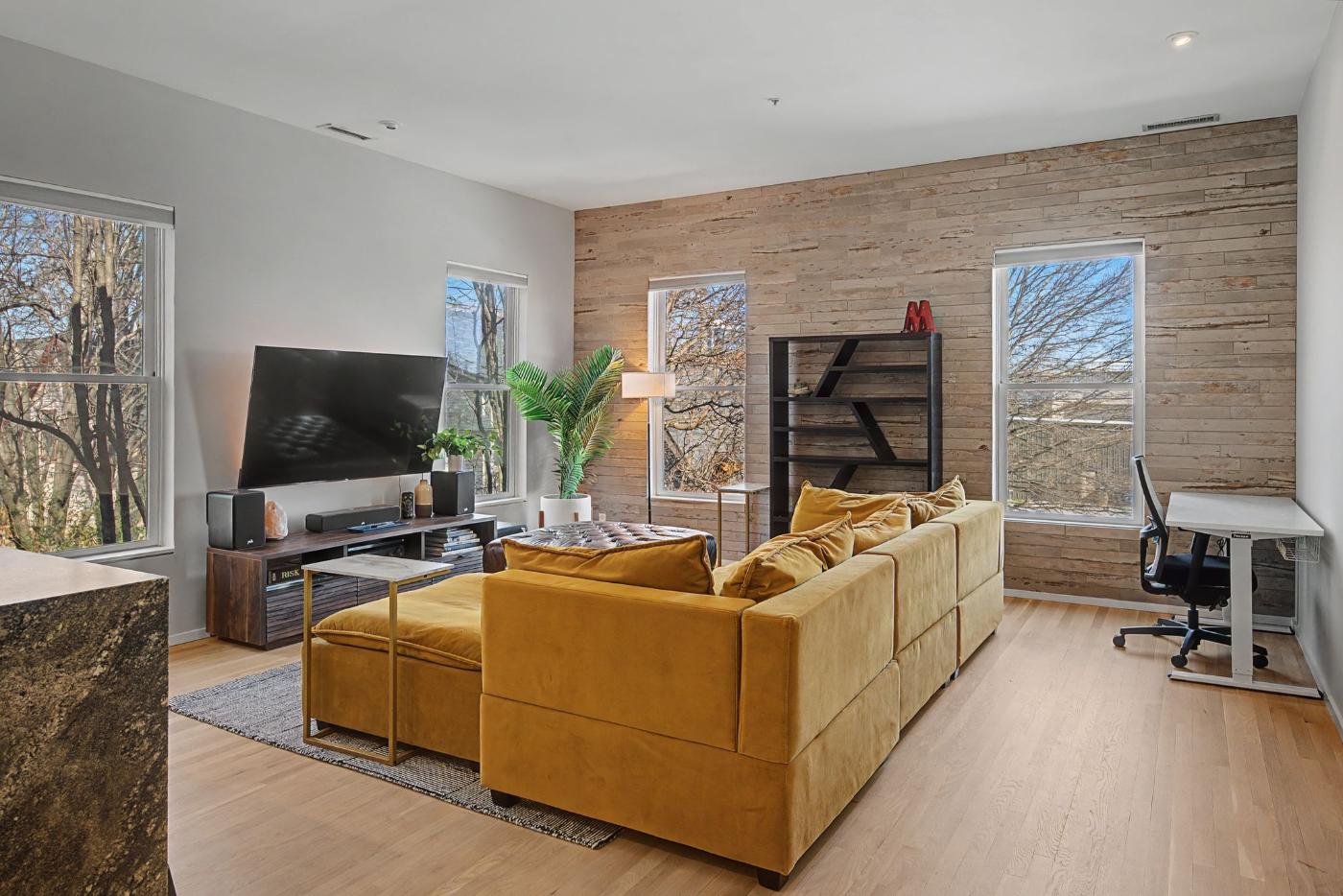 Living area at Residence 414 with a custom wood trim accent wall, wood flooring and tree-filled windows in Historic Germantown Nashville