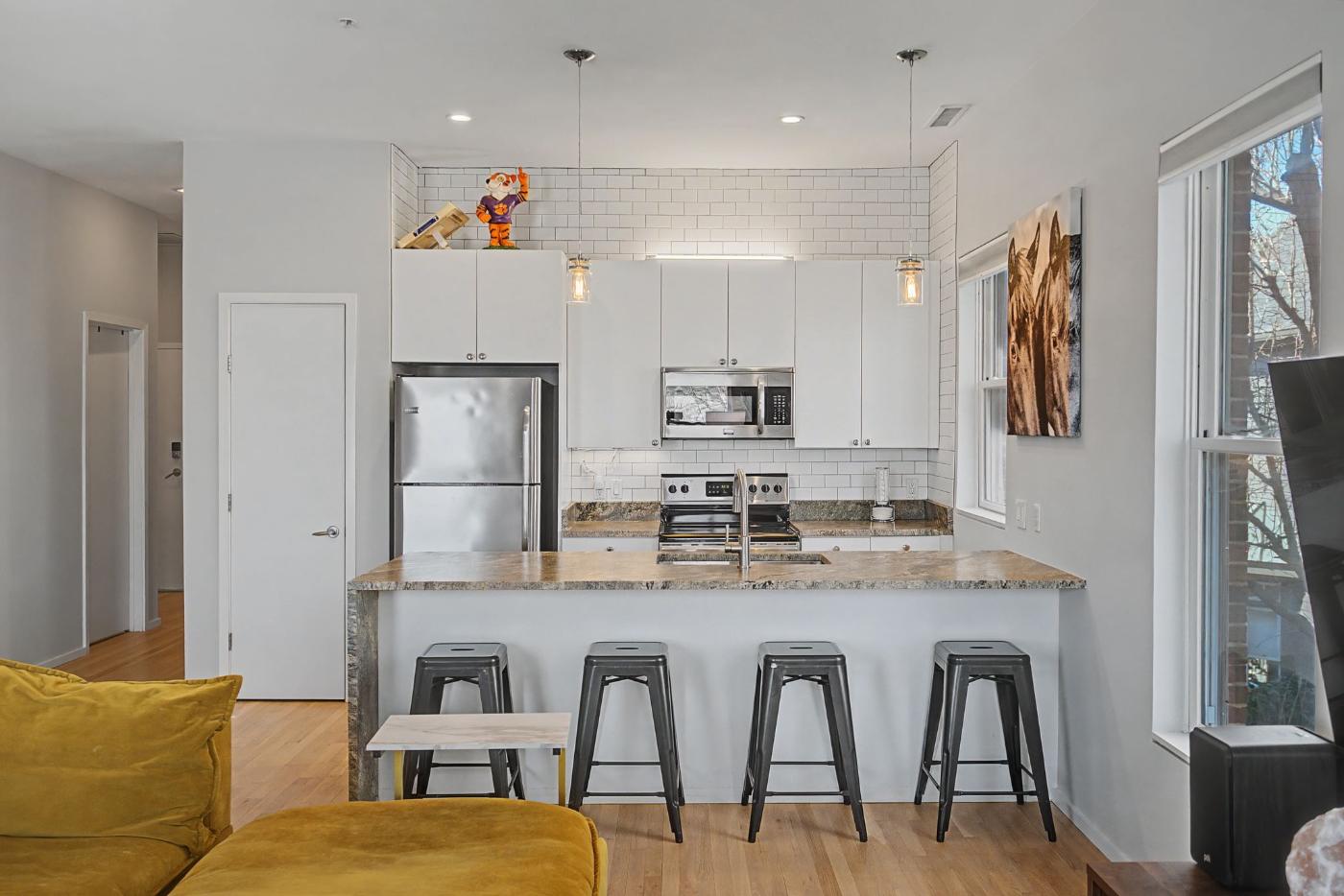 Kitchen at Residence 414 with white cabinetry, subway tile, stainless appliances and a waterfall-edge island with bar seating