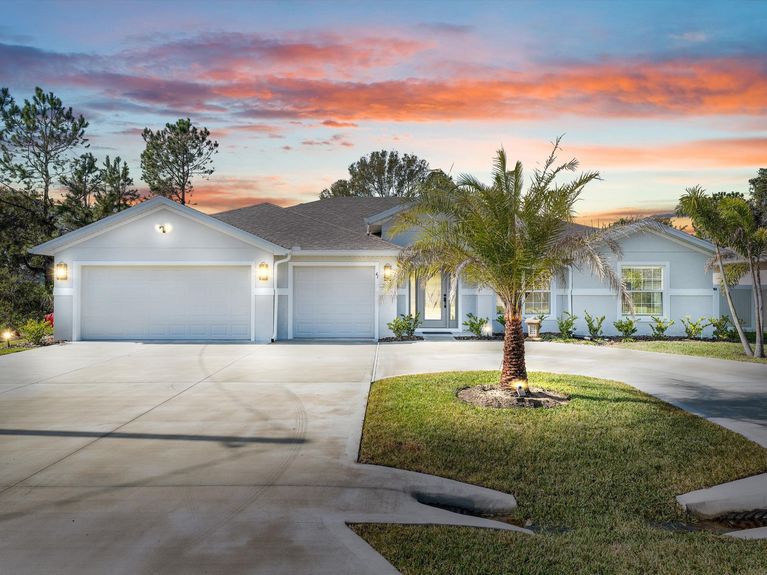 A one-story home in Palm Coast with a circular driveway, palm tree, and a spacious 3-car garage.