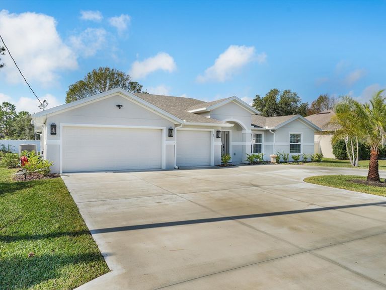 A one-story home in Palm Coast with a circular driveway, palm tree, and a spacious 3-car garage.