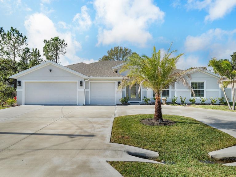 A one-story home in Palm Coast with a circular driveway, palm tree, and a spacious 3-car garage.