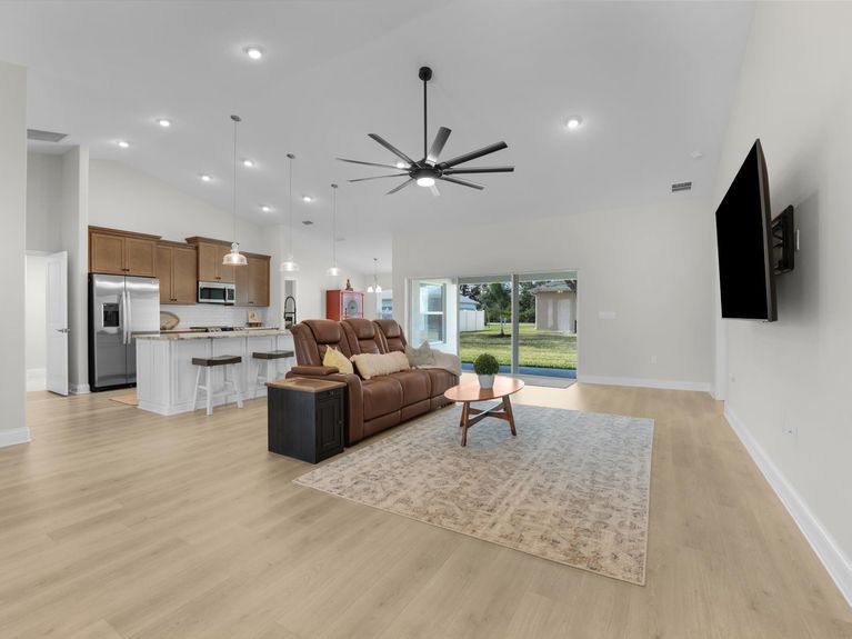 A bright living room in a Palm Coast home featuring high ceilings, a ceiling fan, and sliding doors that lead to the backyard.