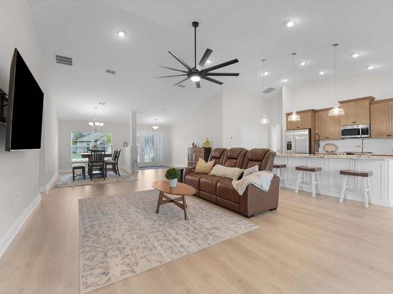 A bright living room in a Palm Coast home featuring high ceilings, a ceiling fan, and sliding doors that lead to the backyard.