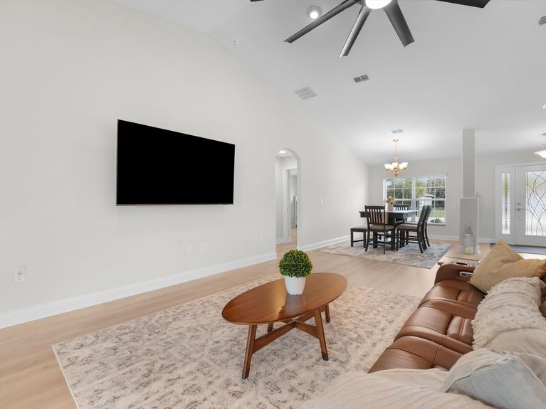 A bright living room in a Palm Coast home featuring high ceilings, a ceiling fan, and sliding doors that lead to the backyard.