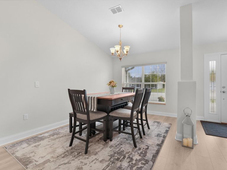 A bright dining room in a Palm Coast home featuring large windows with views of the front yard and stylish decor.