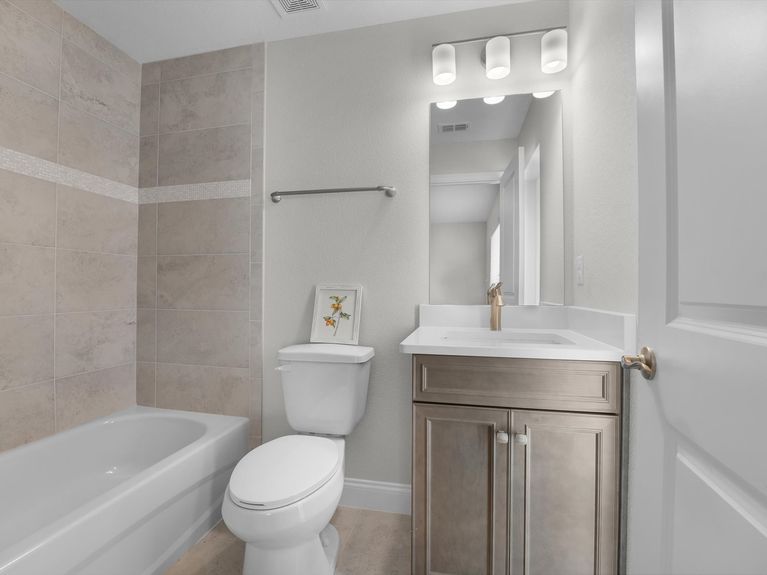 A bright and modern ensuite bathroom featuring a bathtub with tiled surround, a sleek vanity with ample storage, and stylish tile flooring in a Palm Coast home.