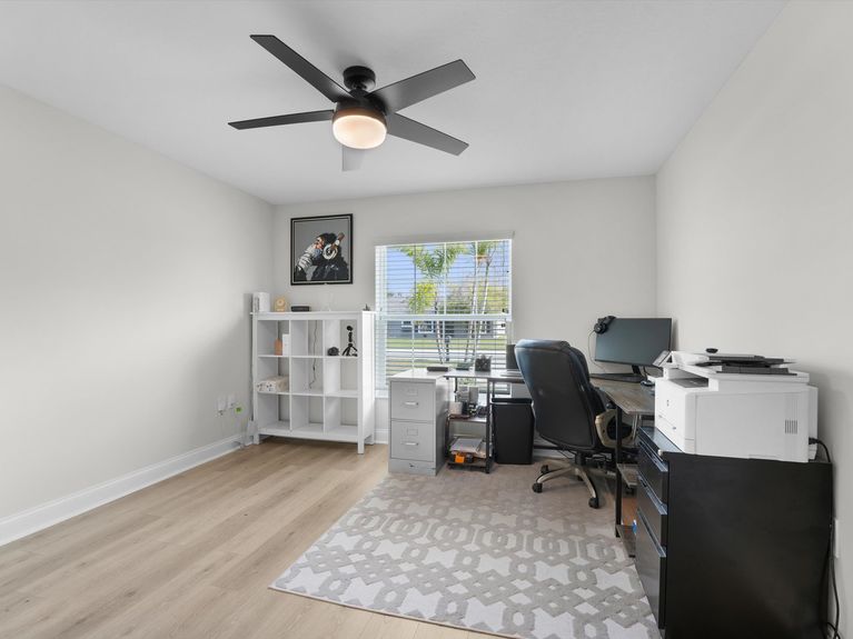 A second bedroom in a Palm Coast home, thoughtfully converted into a functional home office with a desk, shelving, and natural light.