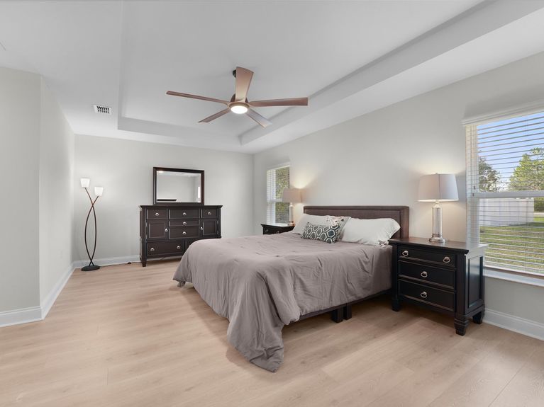 A spacious master bedroom in a Palm Coast home featuring elegant tray ceilings, luxurious LVP flooring, and plenty of room for large furniture.