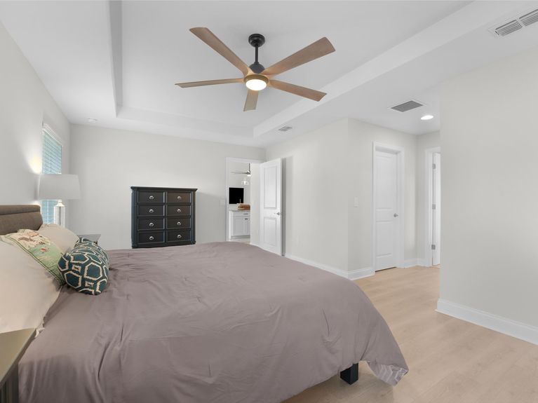 A spacious master bedroom in a Palm Coast home featuring elegant tray ceilings, luxurious LVP flooring, and plenty of room for large furniture.