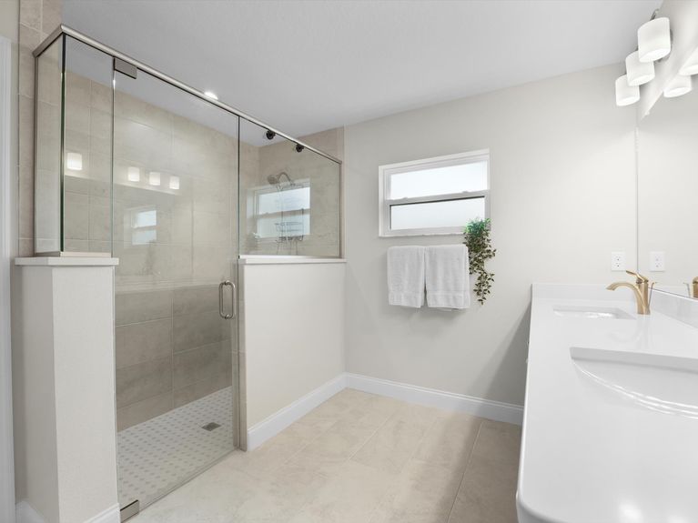 A luxurious primary bathroom in a Palm Coast home featuring a walk-in shower with glass doors, double sinks, and stylish tile flooring.