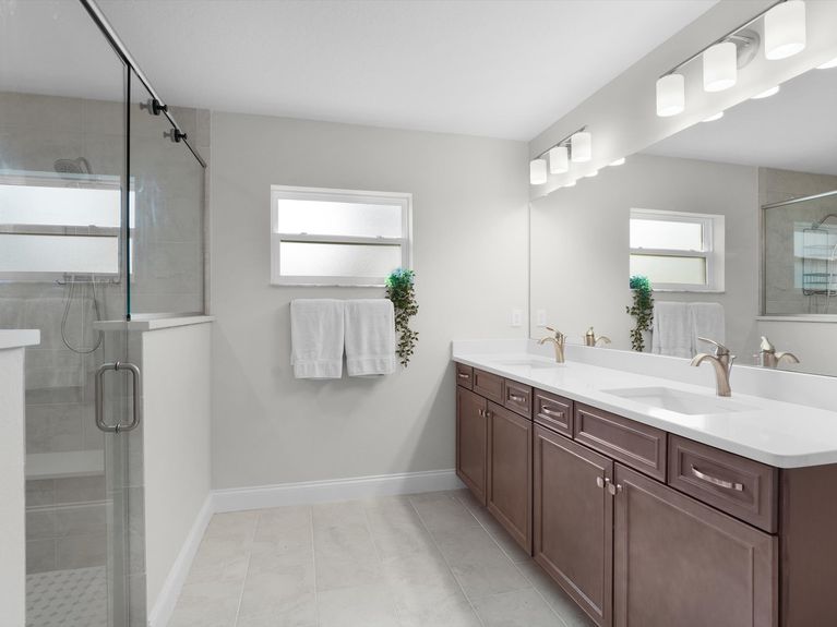 A luxurious primary bathroom in a Palm Coast home featuring a walk-in shower with glass doors, double sinks, and stylish tile flooring.