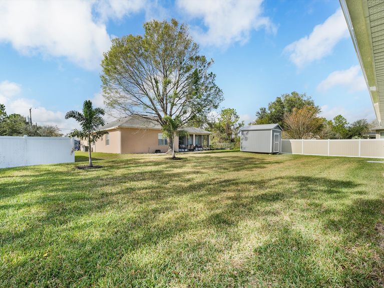 A private backyard with a covered lanai, a mature trees, and a storage shed, in Palm Coast, Florida.