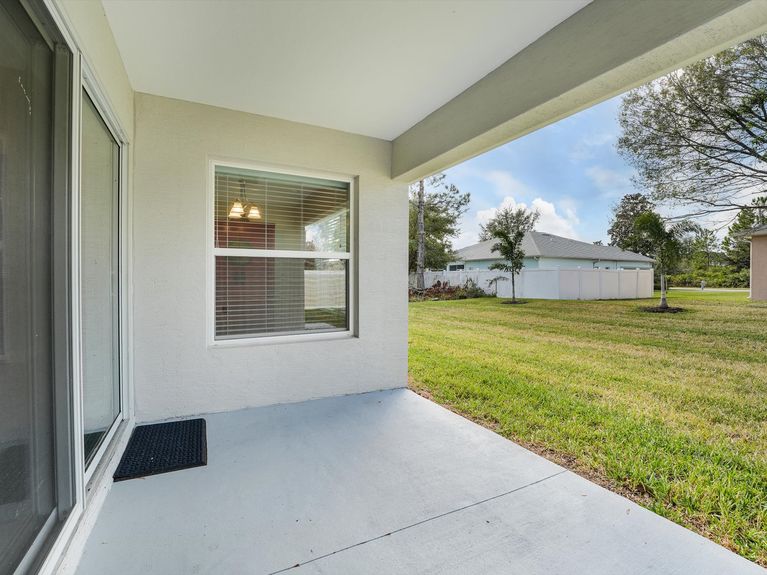 A covered lanai with comfortable seating and a view of the backyard in a Palm Coast, Florida, home.