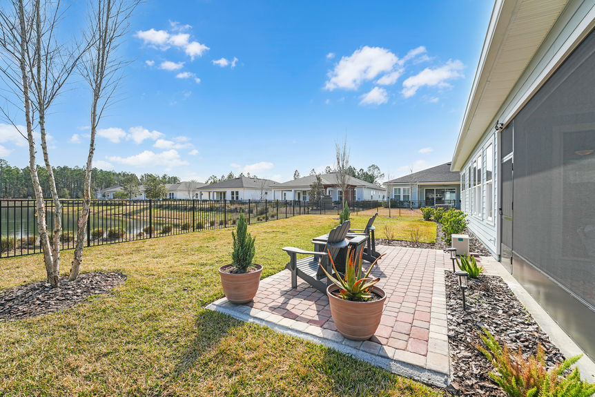 Private fenced backyard at 50 Skyline Lane, featuring a covered patio, lush green space, and peaceful pond views in Reverie at Trailmark, St. Augustine.