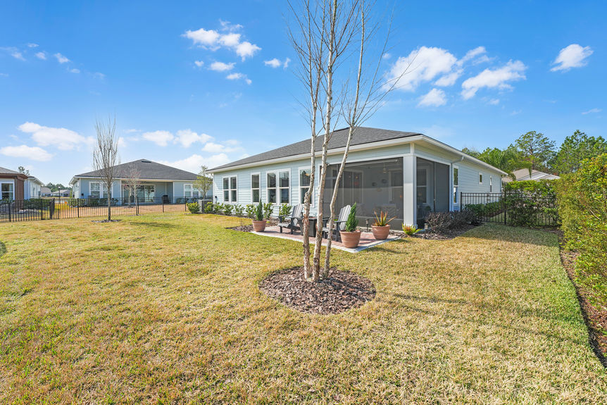 Private fenced backyard at 50 Skyline Lane, featuring a covered patio, lush green space, and peaceful pond views in Reverie at Trailmark, St. Augustine.