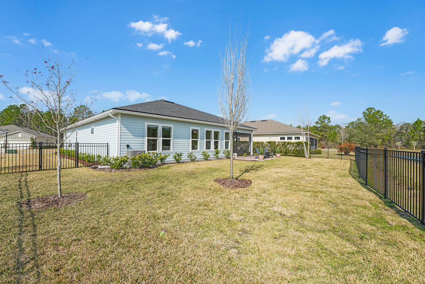 Private fenced backyard at 50 Skyline Lane, featuring a covered patio, lush green space, and peaceful pond views in Reverie at Trailmark, St. Augustine.