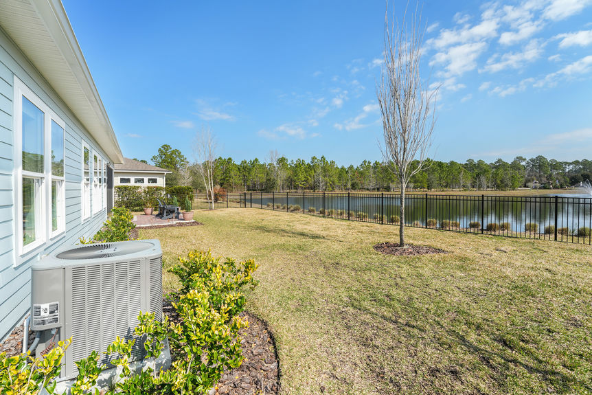 Private fenced backyard at 50 Skyline Lane, featuring a covered patio, lush green space, and peaceful pond views in Reverie at Trailmark, St. Augustine.