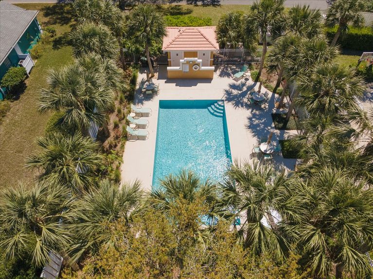 Large, sparkling blue community pool in Anastasia Lakes, surrounded by lush greenery and a relaxing deck area.