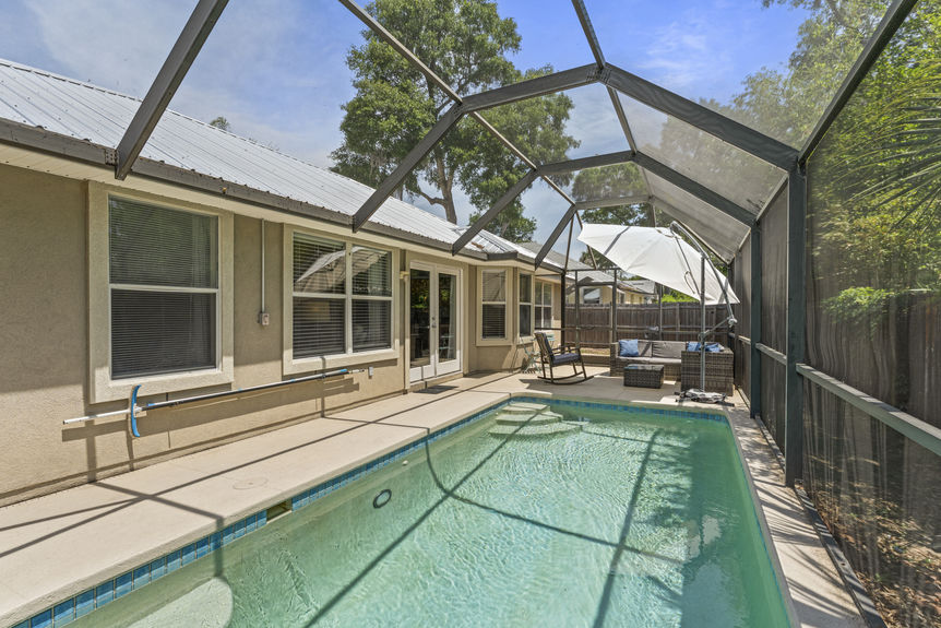 Backyard view of in-ground pool surrounded by privacy fencing and greenery in St. Augustine Florida